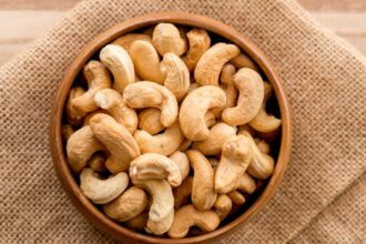 Egy fából készült tálban frissen pörkölt kesudiók láthatók, amelyek ízletes és tápláló nassolnivalók.