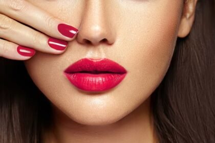 Egy nő arca, élénk piros rúzzsal és manikűrözött körmökkel, amely kiemeli a smink szépségét.