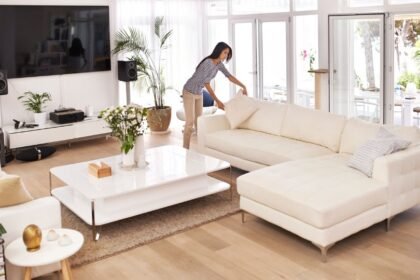 Egy nő rendet rak a világos nappaliban, fehér kanapén párnákat igazít.