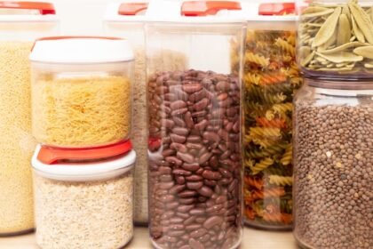 Többféle szárazbab és tészta tárolóedényekben, rendezett konyhai háttérben.