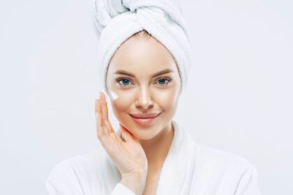 Egy fiatal nő arckrémmel a kezén, törölközővel a fején, mosolyogva néz a kamerába.