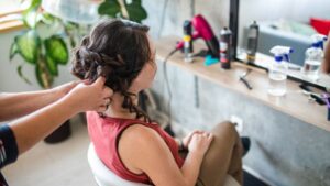 womensway 121 Egy nő ül a széken, miközben a fodrásza éppen frizurát készít neki, a tükörben látható a hajformázás folyamata.