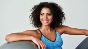 Egy fiatal nő mosolyogva ül egy fitneszlabdán, sportos ruhában, a testmozgás örömét sugallva.