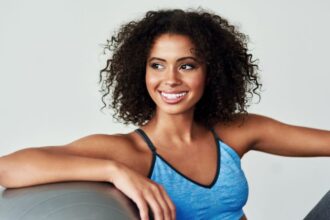 Egy fiatal nő mosolyogva ül egy fitneszlabdán, sportos ruhában, a testmozgás örömét sugallva.