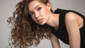 Egy fiatal nő dús, göndör hajjal, természetes sminkkel néz a kamerába.