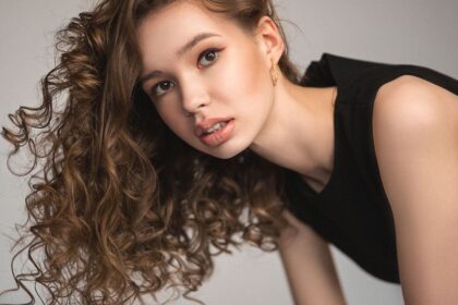 Egy fiatal nő dús, göndör hajjal, természetes sminkkel néz a kamerába.