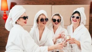 Négy barátnő fürdőköpenyben, napszemüvegben pezsgőt koccintva, vidám hangulatban.