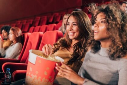 Két fiatal nő ül a moziban, popcornnal a kezükben, élvezve a filmet.