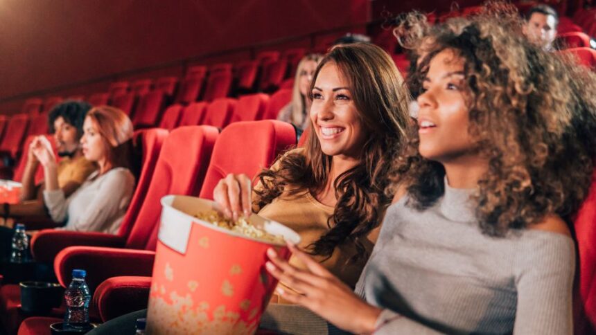 Két fiatal nő ül a moziban, popcornnal a kezükben, élvezve a filmet.