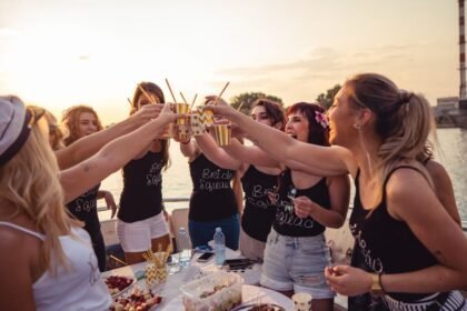 Női csapatépítő esemény a vízen, ahol barátnők koccintanak italokkal naplementében.