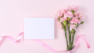 Egy csokor rózsaszín szegfű és egy üres kártya rózsaszín háttéren, tökéletes névnapi köszöntőhöz.