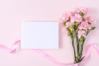 Egy csokor rózsaszín szegfű és egy üres kártya rózsaszín háttéren, tökéletes névnapi köszöntőhöz.