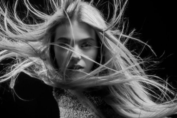 Egy fiatal nő arca látható, hosszú, szőke haja szélben lobog, a háttér fekete.