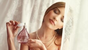 Egy nő finoman parfümöt fúj magára, miközben a fény lágyan megvilágítja az arcát.