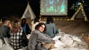 Fiatalok ülnek egy kényelmes, szabadtéri kertmoziban, a vászon előtt filmnézés közben.