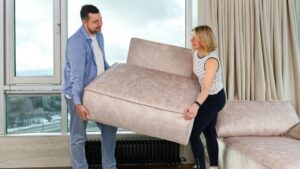 Két ember, egy férfi és egy nő, kanapét emelnek a lakásban, friss energiát hozva az otthonukba.