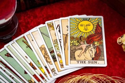 Tarot kártyák, köztük a Nap kártya, egy piros háttér előtt, mellette kristálygömb.