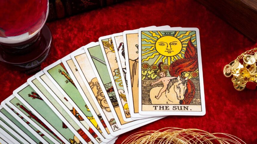 Tarot kártyák, köztük a Nap kártya, egy piros háttér előtt, mellette kristálygömb.