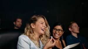 Két nő nevetve nézi a filmet a moziban, popcornnal a kezükben.