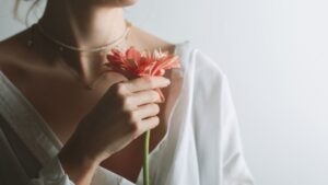 Egy nő, aki fehér blúzt visel, egy szép virágot tart a kezében, sugárzik belőle a nőiesség és a belső erő.