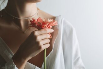 Egy nő, aki fehér blúzt visel, egy szép virágot tart a kezében, sugárzik belőle a nőiesség és a belső erő.