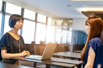 Két nő ül egy modern irodában, egy laptop előtt, beszélgetve a karrierlehetőségeikről.