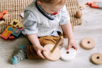 Egy kisgyermek játszik fa játékokkal, körülötte színes építőelemek. Az utazás során hasznos játékokkal foglalja el magát.