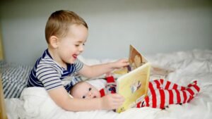 Egy nagyobb fiú boldogan olvas egy mesekönyvet a kisbaba mellett, aki figyelmesen nézi őt.