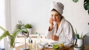 Egy nő arcmaszkot használva ül egy asztalnál, körülötte bőrápoló termékek és friss zöldségek.