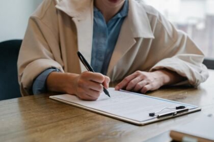 Egy szülő kézzel ír egy szülői igazolást egy asztalon, mellette irattartó.