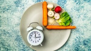 Egy tányéron zöldségek, rizs és egy óra, ami az időszakos böjtöt szimbolizálja.