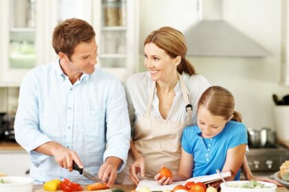 Egy család közösen főz a konyhában, a szülők és a gyermek együttműködnek az étkezés előkészítésében.