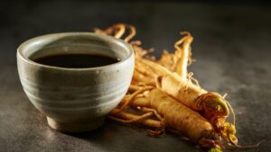 Egy kerámia csésze ginzeng teával, mellette friss ginzeng gyökerek.