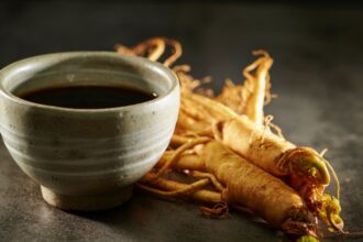 Egy kerámia csésze ginzeng teával, mellette friss ginzeng gyökerek.