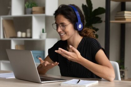 Egy fiatal nő vidáman beszélget a laptopján, fejhallgatóval, távkapcsolatban.