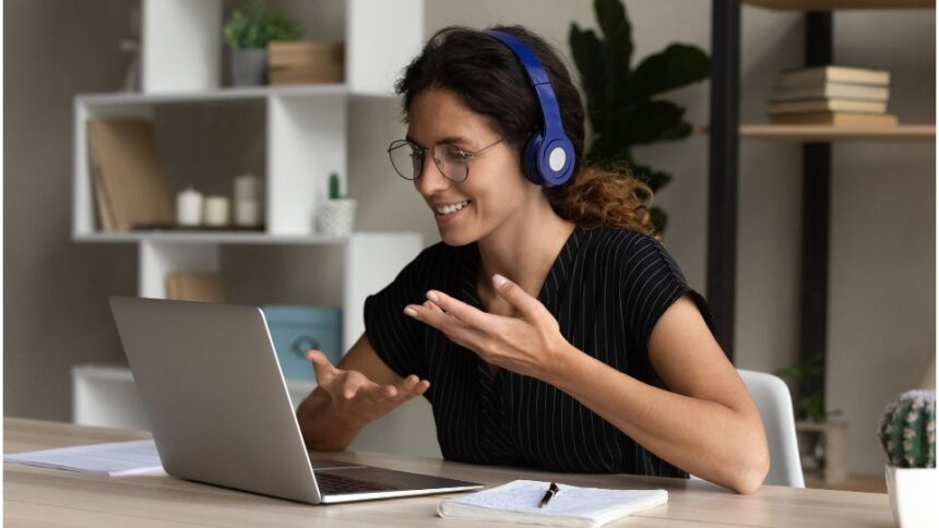 Egy fiatal nő vidáman beszélget a laptopján, fejhallgatóval, távkapcsolatban.