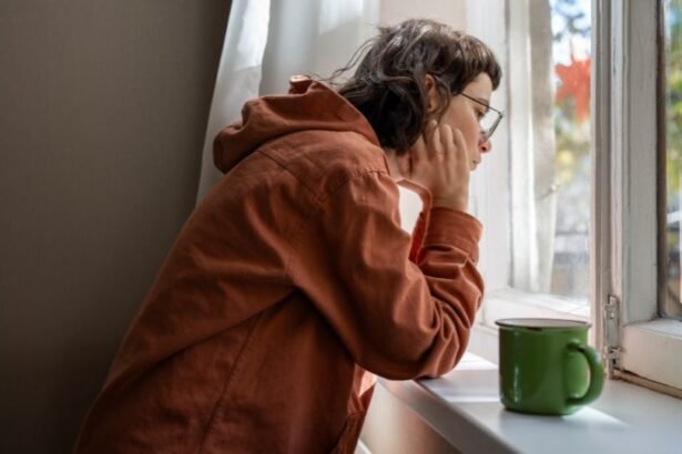 Egy introvertált nő az ablak mellett ül, gondolkodva néz kifelé, kezében egy zöld bögre.