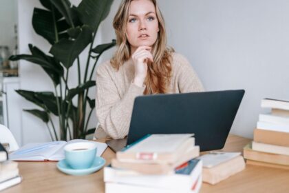Mi irányítja a gondolkodásod? 2 Egy fiatal nő gondolkodik a laptopja előtt, könyvek és egy csésze kávé mellett ülve.