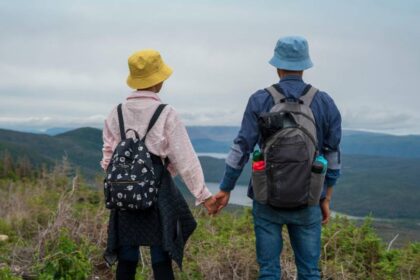 Két túrázó, akik kézen fogva állnak egy hegytetőn, gyönyörű tájat nézve.