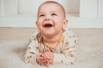 Egy boldog csecsemő fekszik a puha szőnyegen, mosolyogva néz fel.
