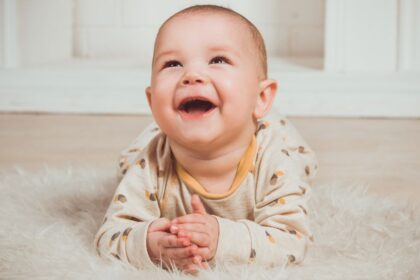 Egy boldog csecsemő fekszik a puha szőnyegen, mosolyogva néz fel.