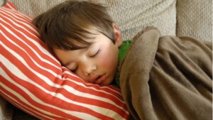 womensway 126 Egy kisfiú békésen alszik egy piros csíkos párnán, takaróba burkolózva.
