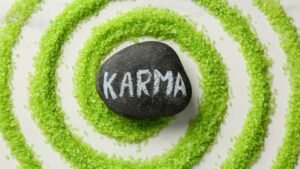 Egy fekete kő, amelyen a 'KARMA' felirat látható, zöld cukorszirup spirálban elhelyezve.