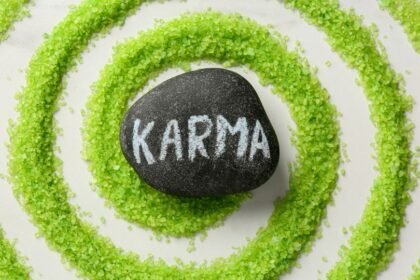 Egy fekete kő, amelyen a 'KARMA' felirat látható, zöld cukorszirup spirálban elhelyezve.