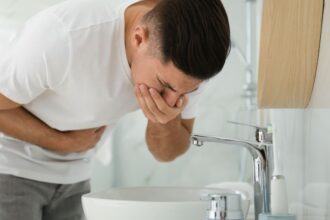 Egy férfi hányingert érezve a mosdó fölé hajol, hasi fájdalommal küzd.