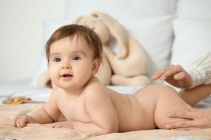 Egy mosolygó baba fekszik egy puha törölközőn, míg egy kéz óvatosan simogatja a popsiját.