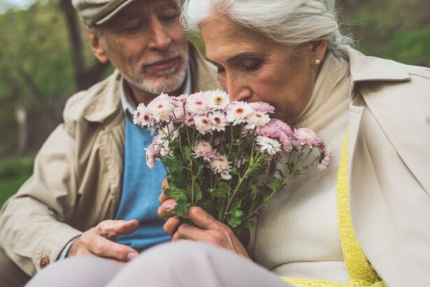 Idős pár ül egy parkban, a nő virágcsokrot szagol, míg a férfi figyeli őt.