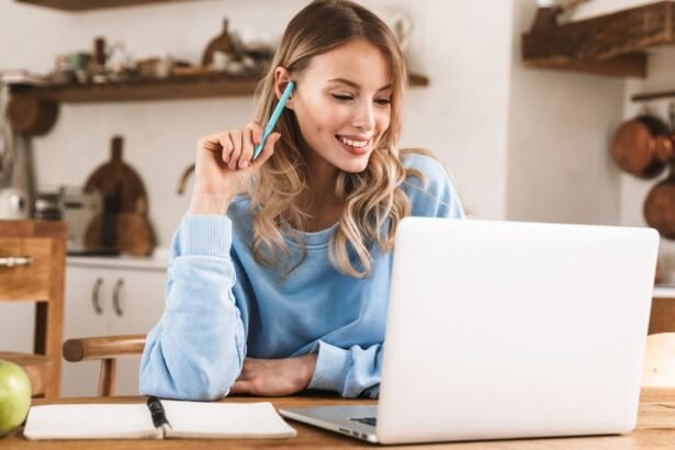 Egy fiatal nő mosolyogva ül egy asztalnál, laptop előtt, miközben egy ceruzát tart a kezében.