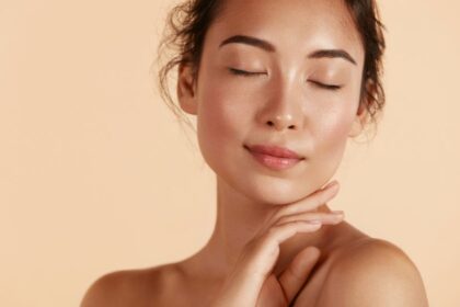 Egy fiatal nő zárt szemmel, sima és ragyogó bőrrel, az arcát finoman simogatja.