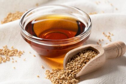 Egy kis üvegben szezámolaj látható, mellette szezámmagokkal teli fakanál.